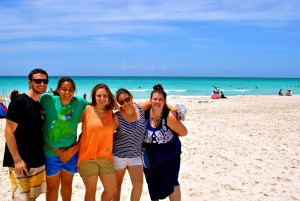 four young women stand on a beach with the ocean behind them